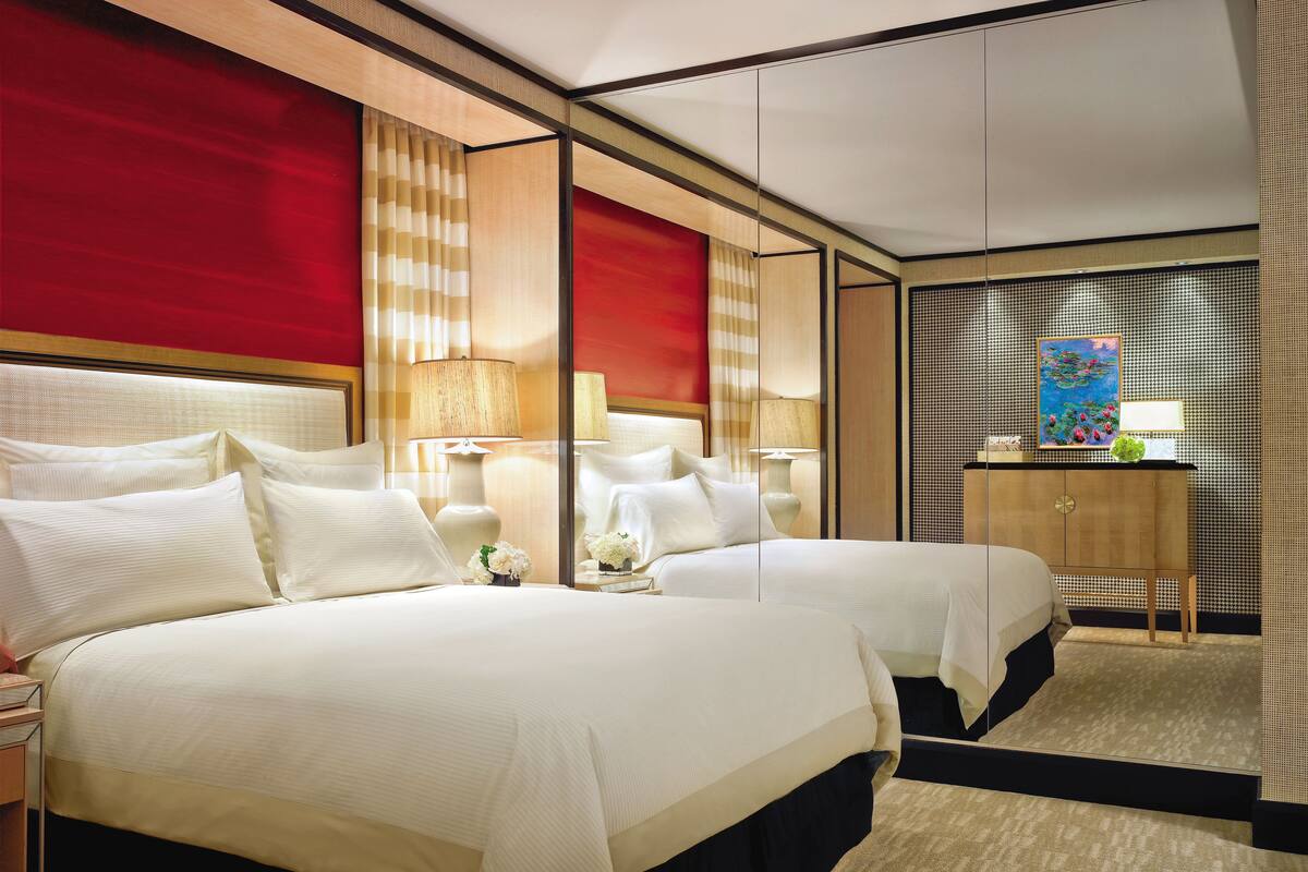 A hotel room with two beds, a large mirror, and a view of the cityscape.