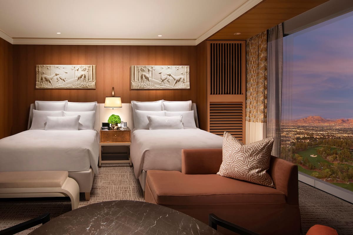 A hotel room with two beds, a sofa, a small table, and a view of a cityscape.