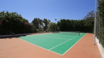 An outdoor tennis court with a green playing surface and a red surrounding area.
