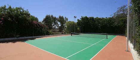 An outdoor tennis court with a green playing surface and a red surrounding area.