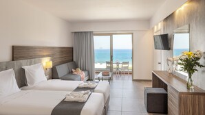 Habitación de hotel con dos camas, un sofá, televisión, una mesa de comedor con sillas y vista al océano.