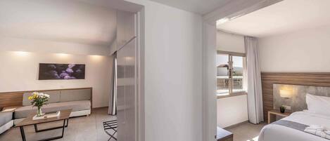 A modern hotel room with a bed, a sofa, a coffee table, and a painting on the wall.