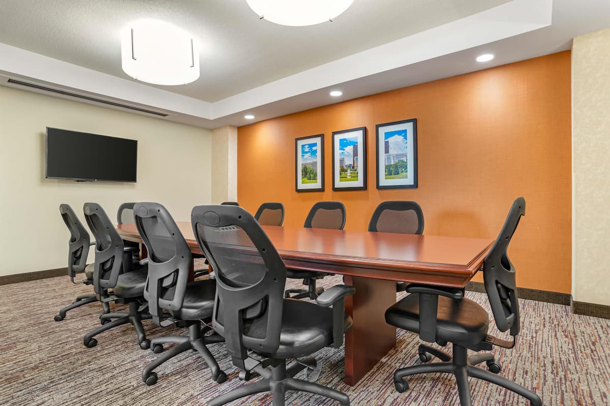 A conference room with a long table, six chairs, a flat-screen TV, and three framed pictures on the wall.