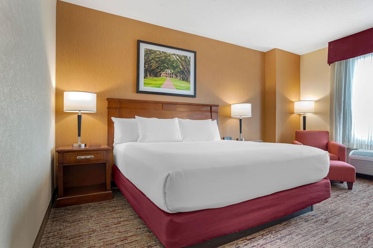 A hotel room with a large bed, two bedside tables, a red armchair, and a framed picture on the wall.