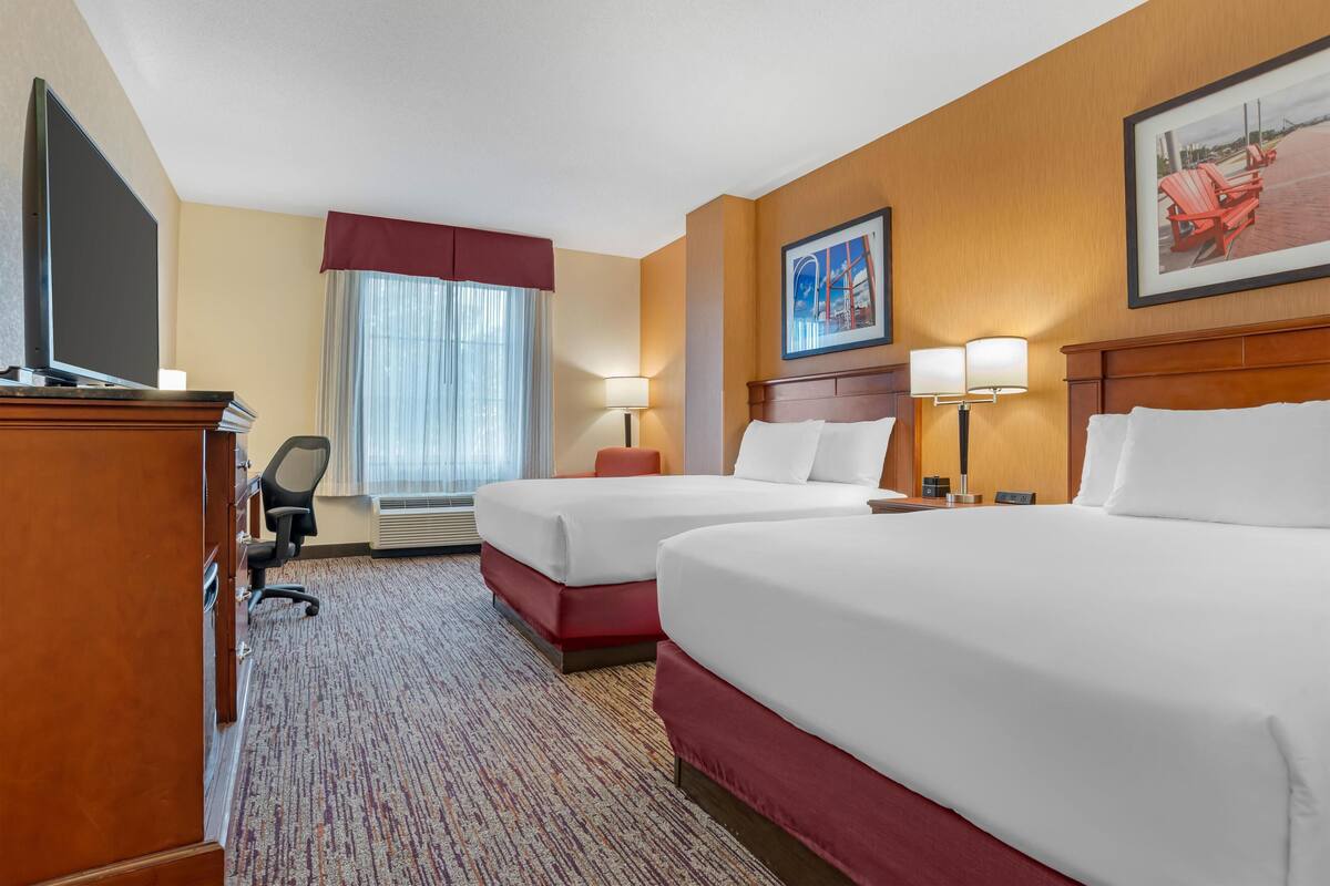 A hotel room with two beds, a desk with a TV, a chair, a lamp, and a painting on the wall.