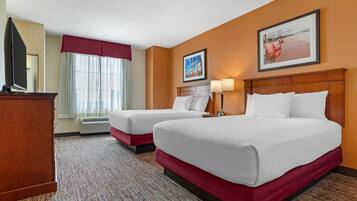A hotel room with two beds, a TV, a desk, and a window with curtains.
