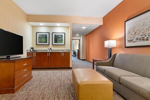 Habitación de hotel con televisión de pantalla plana, muebles de madera, sofá, lámpara y cuadros en las paredes.