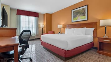 A hotel room with a large bed, a desk with a chair, two bedside lamps, a TV, and a window with curtains.