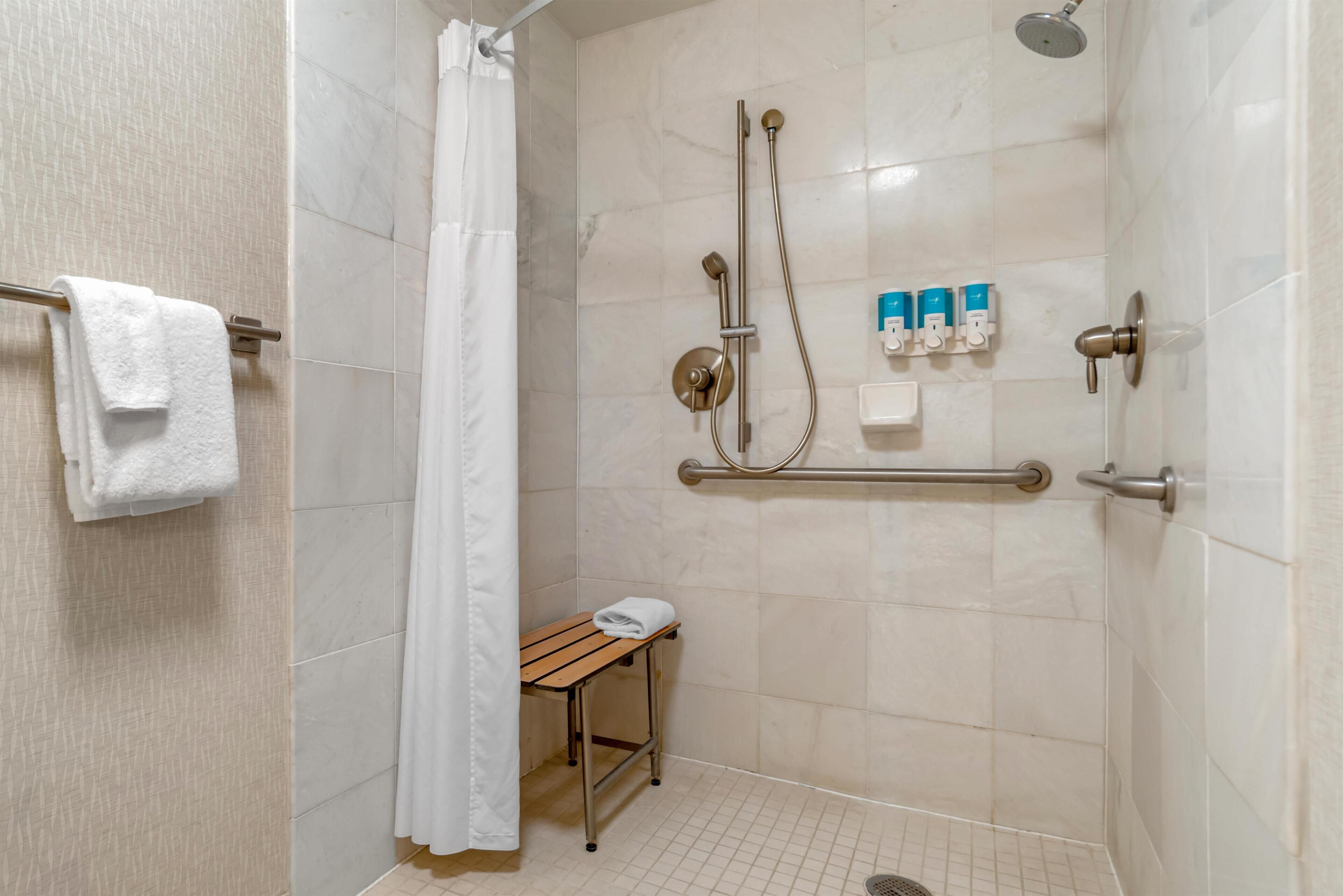 A shower area with a grab bar, a small table with a towel, and a showerhead.