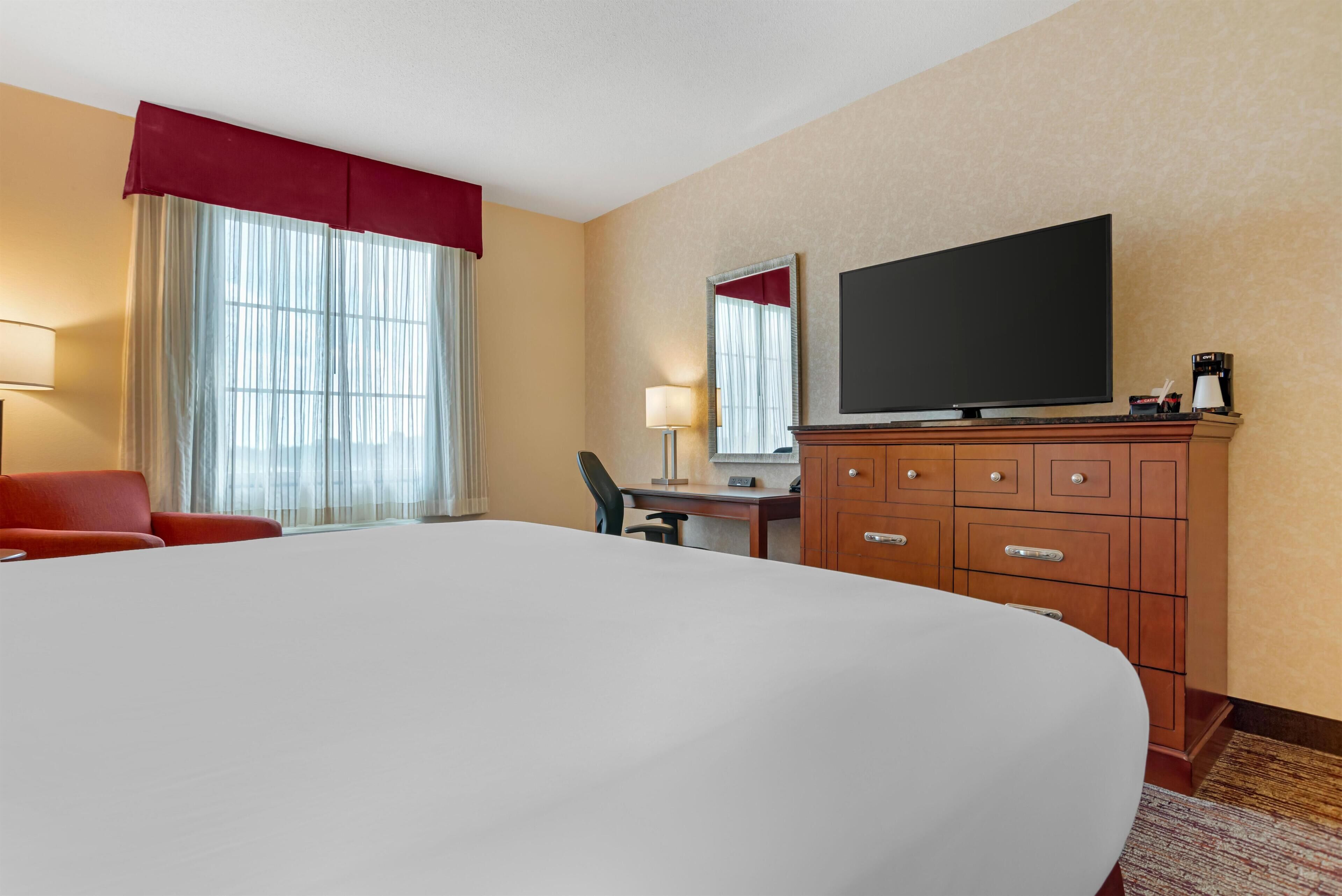 A hotel room with a large bed, a desk with a chair, a television, and a wardrobe.