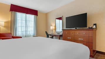 A hotel room with a large bed, a desk with a chair, a television, and a wardrobe.