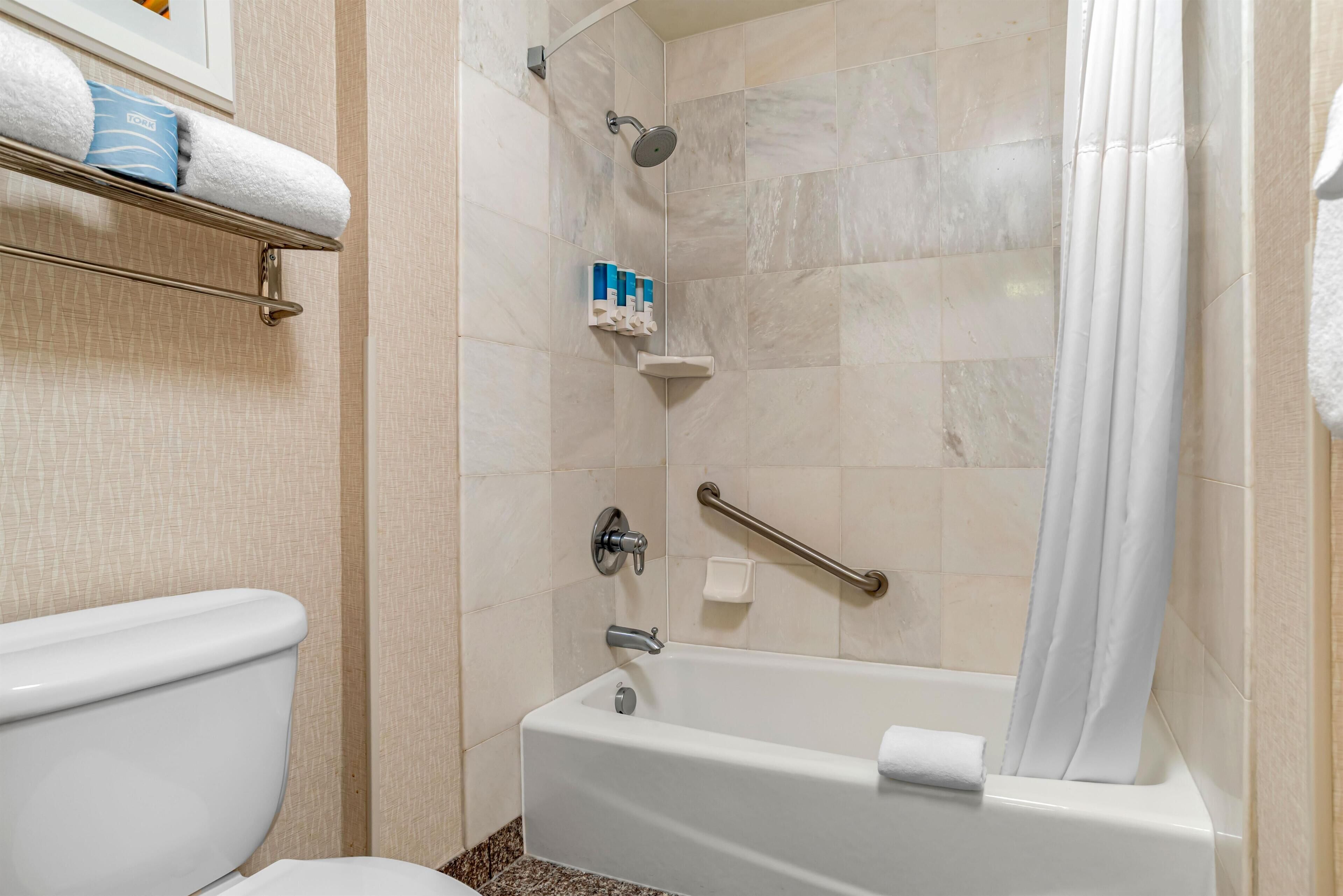 Une salle de bain comprenant des toilettes, une douche équipée d’une barre d’appui et une baignoire.