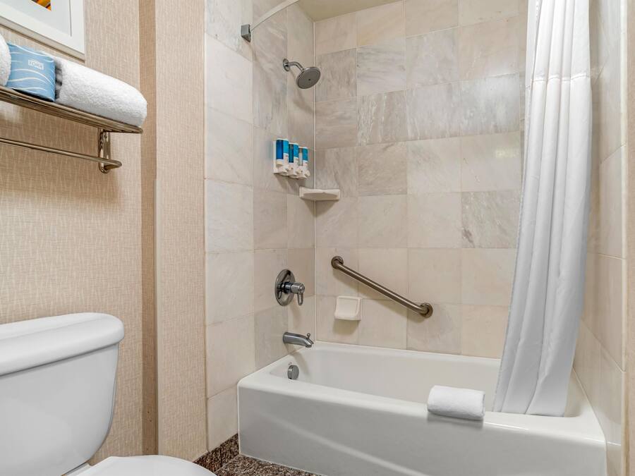 Une salle de bain comprenant des toilettes, une douche équipée d’une barre d’appui et une baignoire.