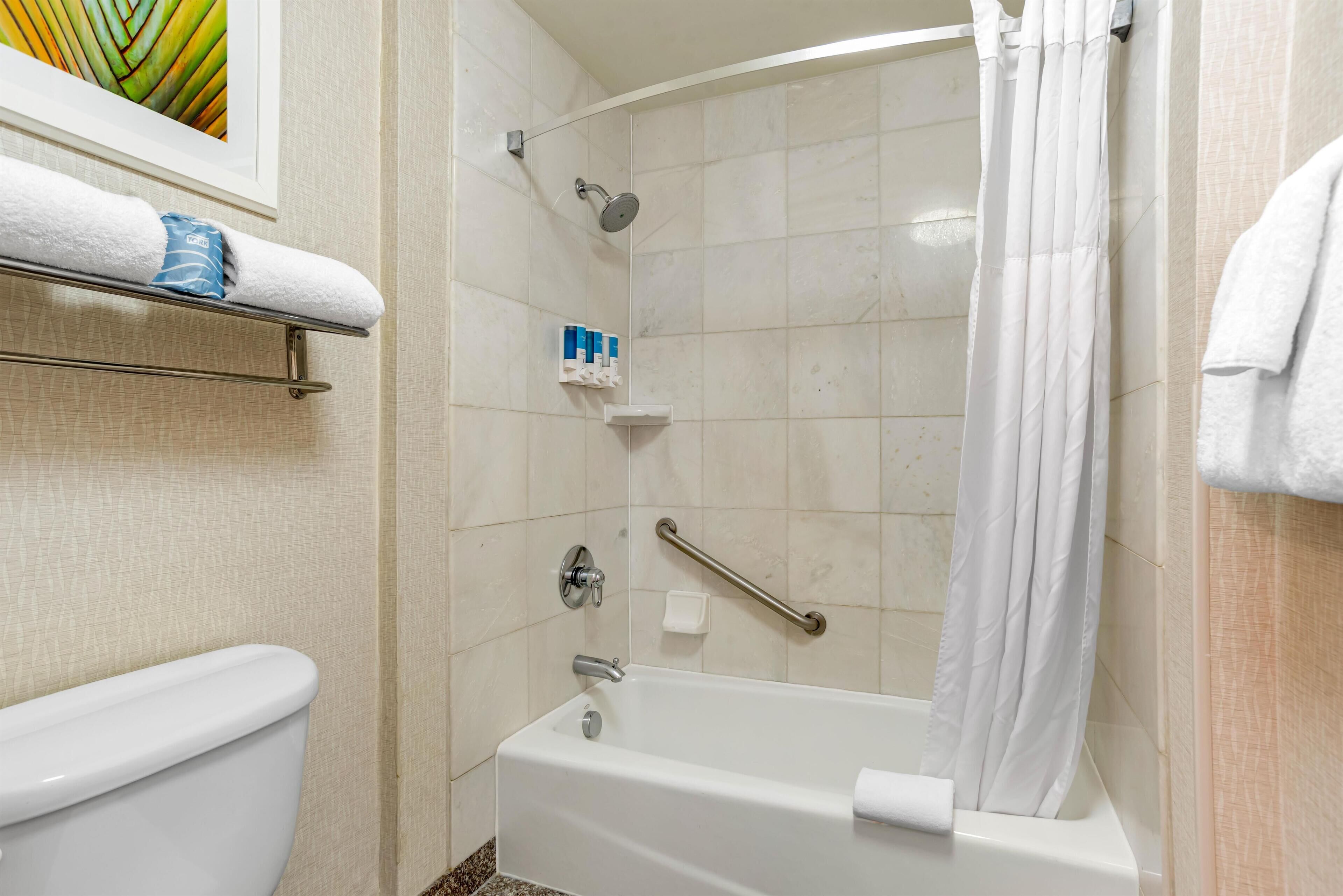 A bathroom with a white bathtub, a shower with a handheld showerhead, a grab bar, and a towel rack with a folded towel.