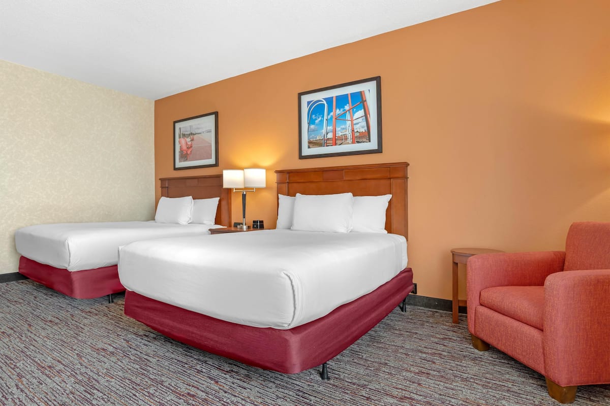 A hotel room with two beds, a red accent wall, and two framed pictures.