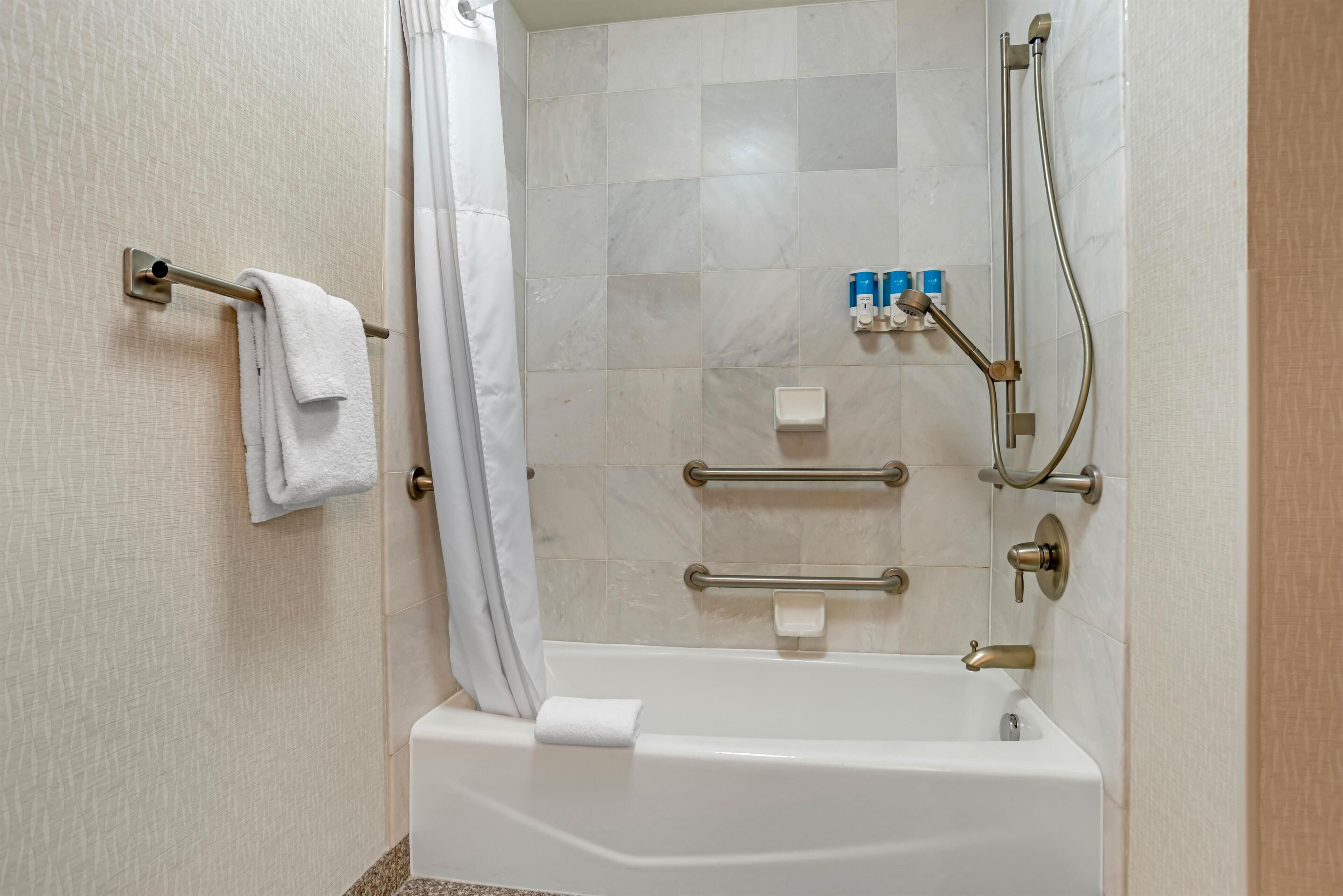 A bathroom with a bathtub, a towel rack, a shower head, and a handrail.