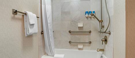 A bathroom with a bathtub, a towel rack, a shower head, and a handrail.