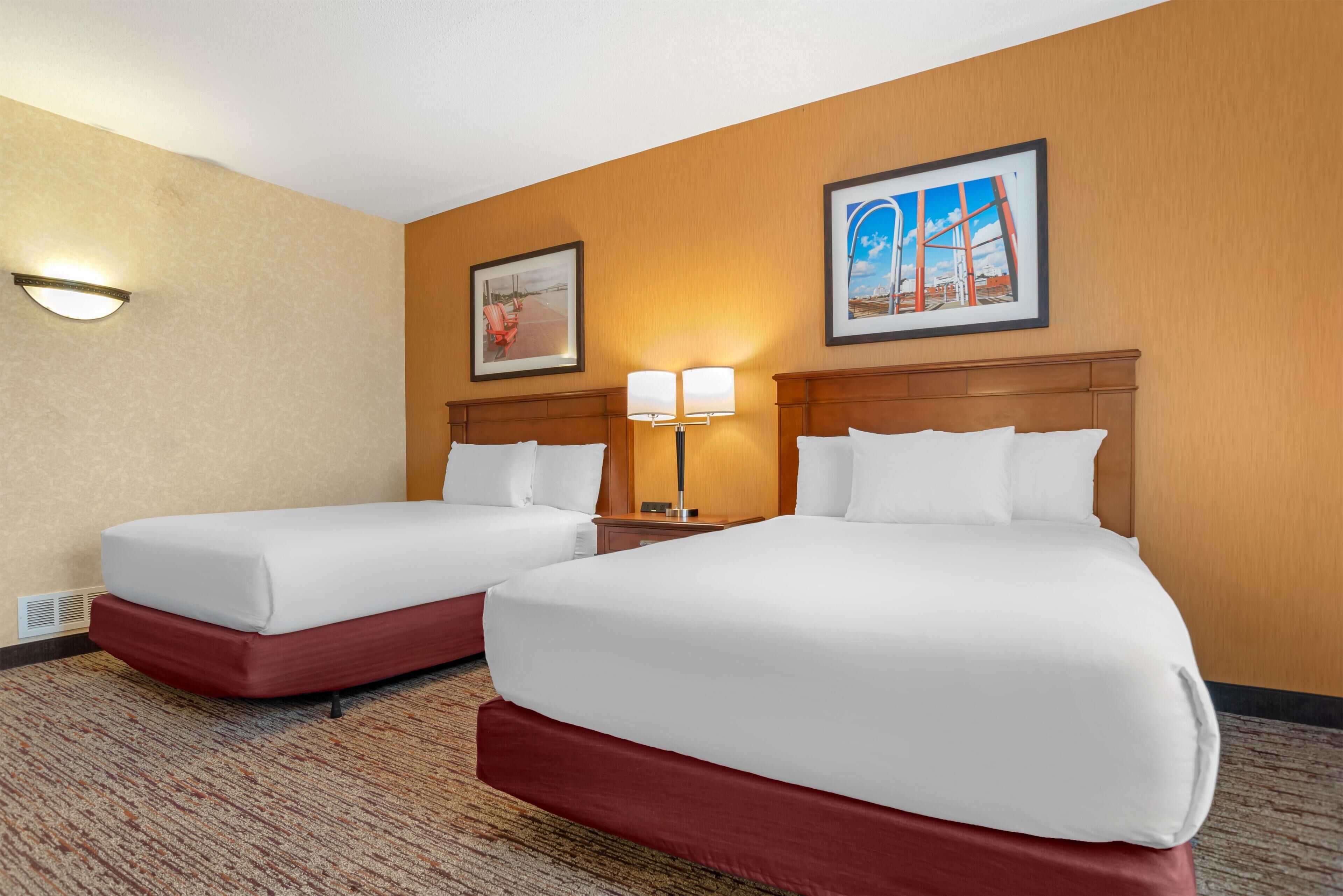 Habitación de hotel con dos camas, piso alfombrado y dos lámparas de pared.