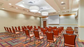A conference room with rows of orange chairs, a carpeted floor, and a projector screen on the wall.