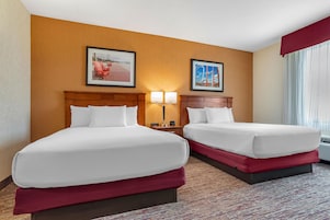 Habitación de hotel con dos camas, una mesita de noche con lámpara y dos cuadros en la pared.