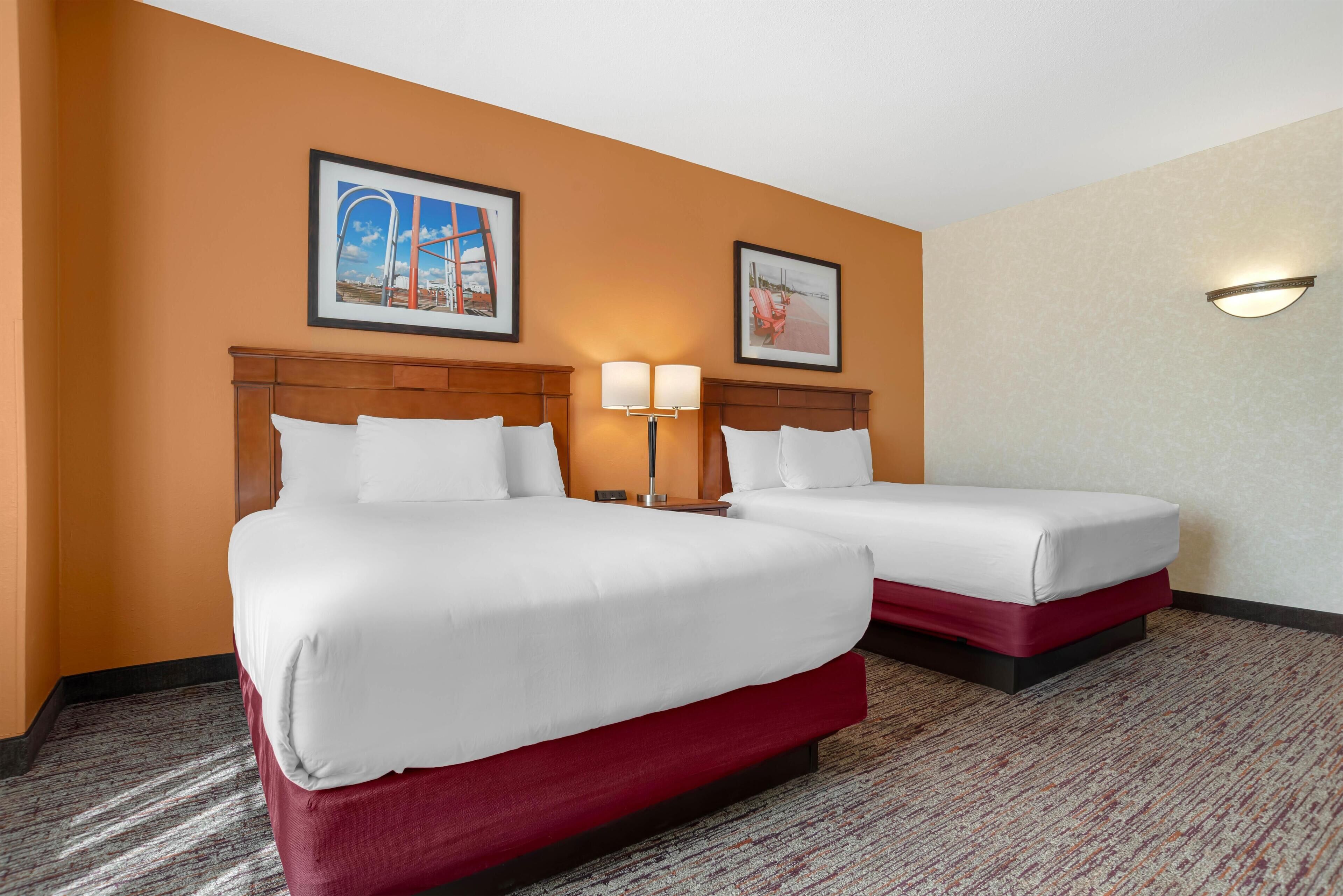 A hotel room with two beds, a carpeted floor, and two framed pictures on the wall.