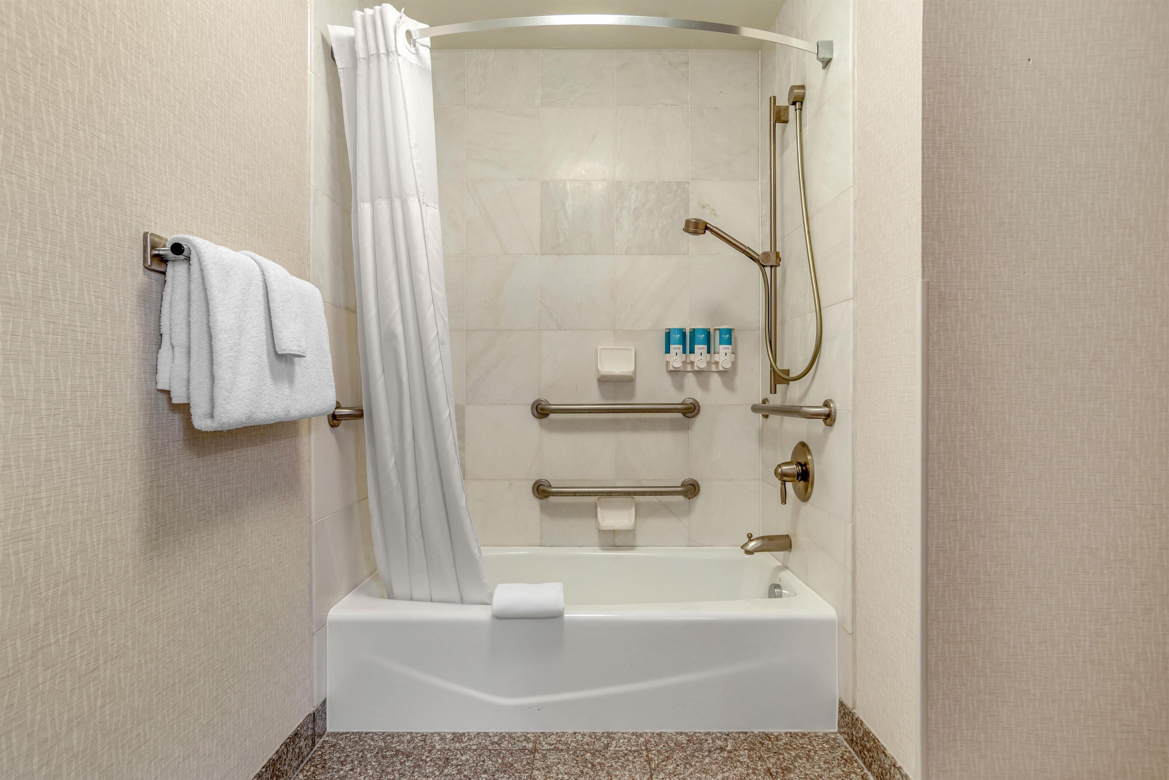 A modern bathroom with a bathtub, shower, and handrails.