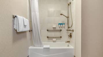 A modern bathroom with a bathtub, shower, and handrails.