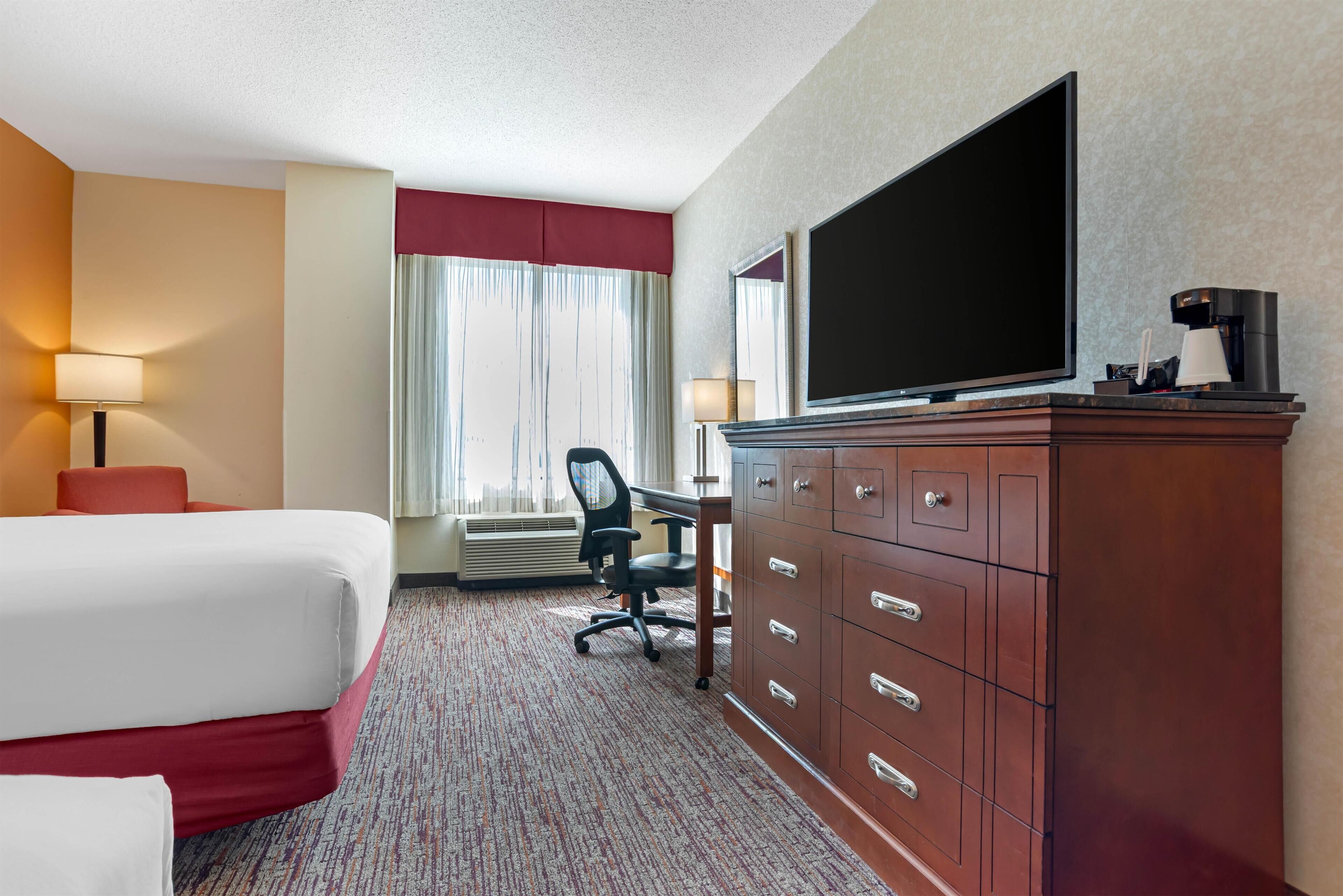 A hotel room with a bed, desk, chair, television, and a wardrobe.