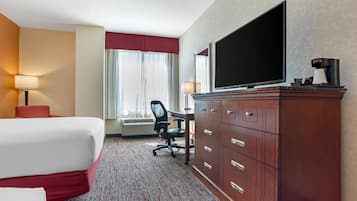 A hotel room with a bed, desk, chair, television, and a wardrobe.
