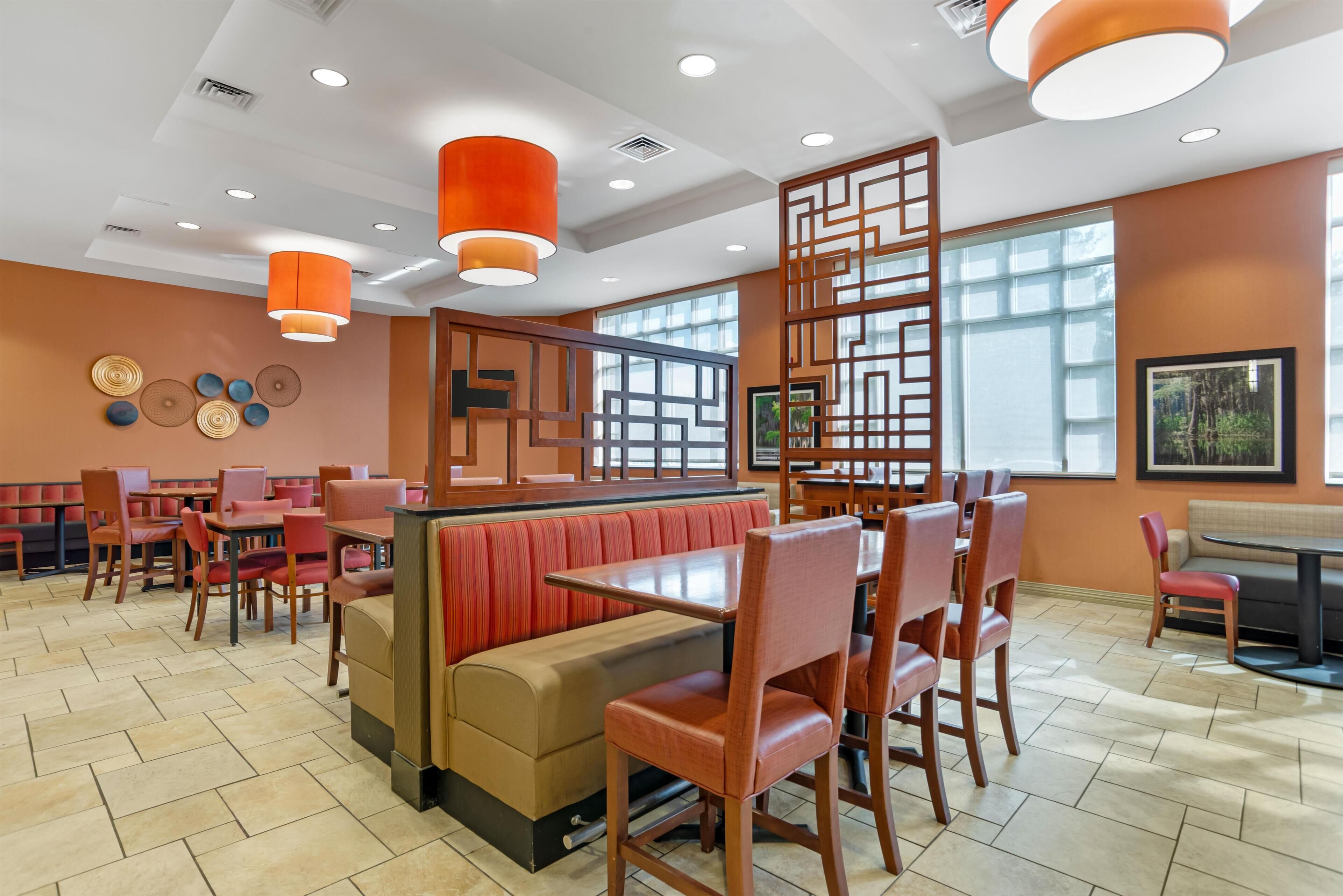 A restaurant with booths and tables, wooden chairs, and orange pendant lights.