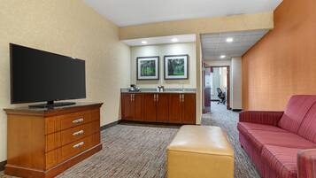 Une chambre d’hôtel équipée d’un téléviseur à écran plat, d’une armoire en bois, d’une kitchenette et d’un canapé à rayures rouges.