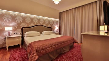 Quarto de hotel com uma cama grande, duas mesas de cabeceira com luminárias, uma escrivaninha com cadeira, um espelho grande e uma televisão.