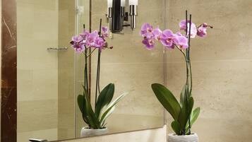 Um banheiro com pia de mármore, um espelho e duas orquídeas em um vaso listrado.
