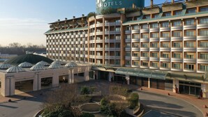 A large hotel with multiple floors, a central courtyard, and a distinctive green dome structure. - UNA Hotels Expo Fiera Milano (Pero)