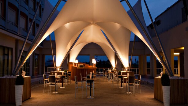 An outdoor dining area with a central bar, surrounded by tables and chairs, under a large tent structure. - UNA Hotels Expo Fiera Milano (Pero)