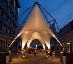An outdoor dining area with a central bar, surrounded by tables and chairs, under a large tent structure. - UNA Hotels Expo Fiera Milano (Pero)