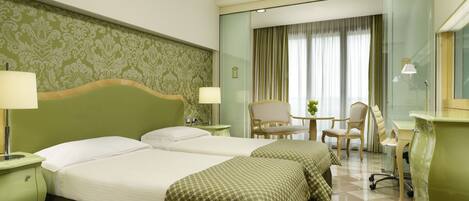 A hotel room with two beds, a desk, a chair, and a small table.