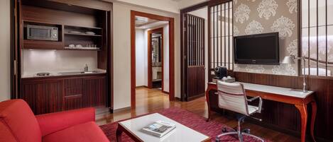 Una habitación de hotel moderna con kitchenette, televisión, sofá rojo y escritorio.