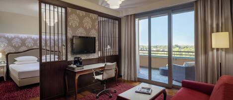 A hotel room with a bed, desk, chair, TV, and a balcony with outdoor furniture.
