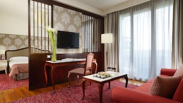 Une chambre d’hôtel avec un lit, un bureau avec une télévision, un canapé rouge et une table à manger avec un tapis rouge.