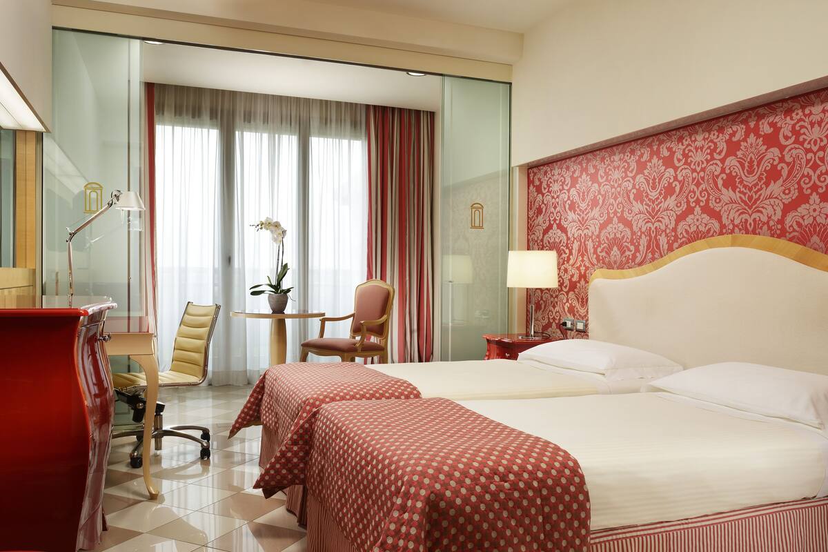 Une chambre d’hôtel avec deux lits, un bureau, une chaise et une petite table avec une lampe.