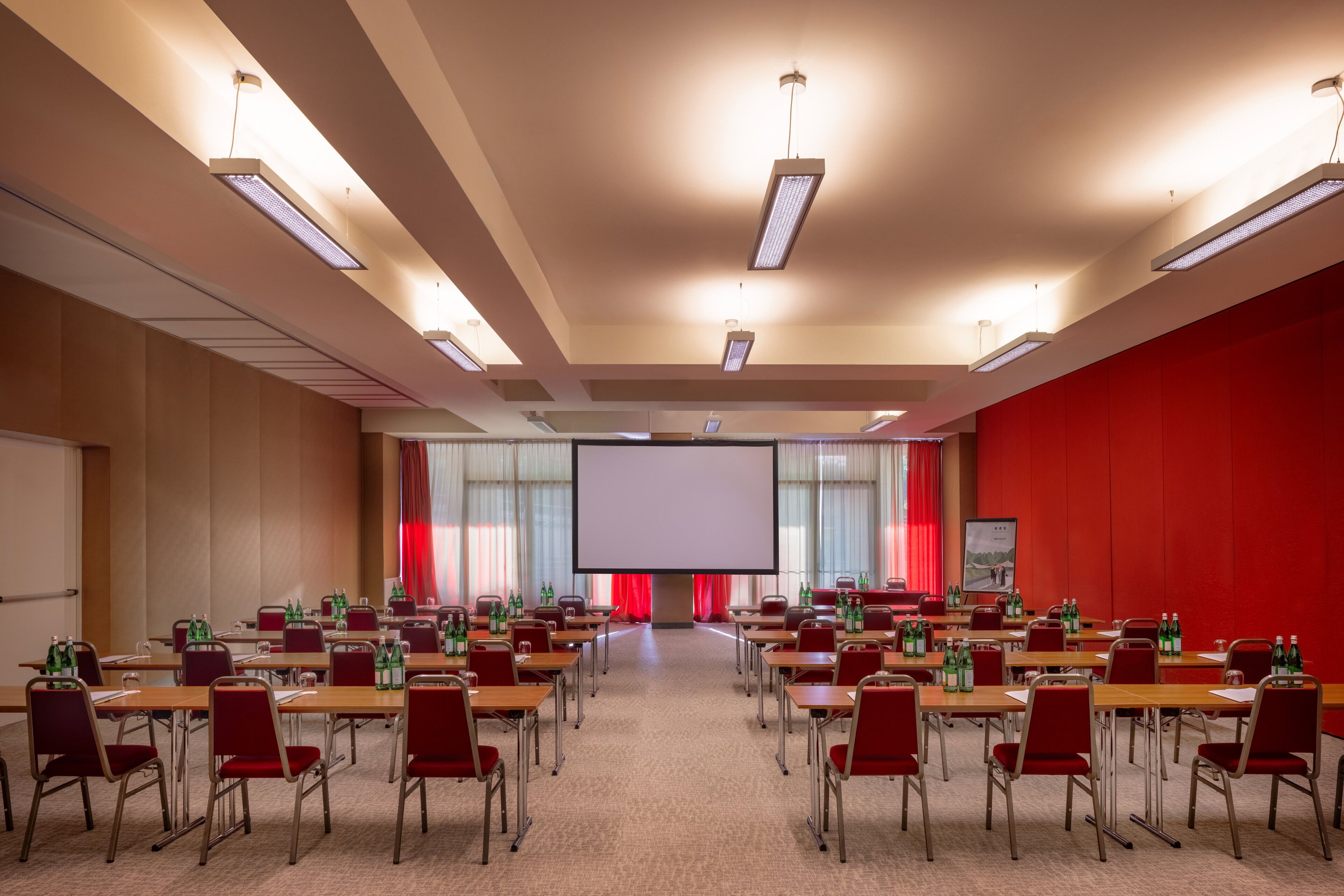 A conference room with multiple tables and chairs, a large screen at the front, and red walls.