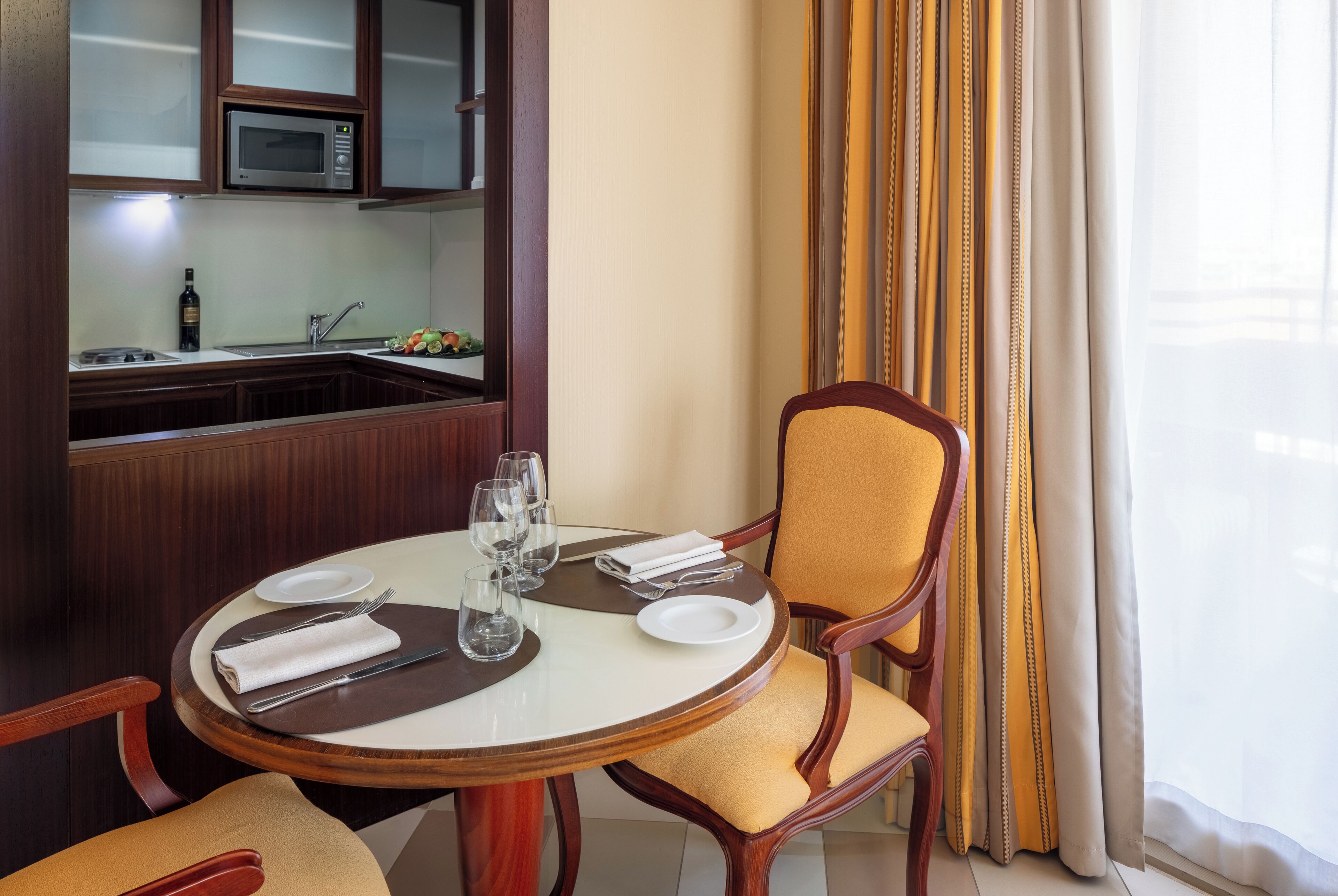 A dining area with a round table, chairs, and a kitchen in the background.