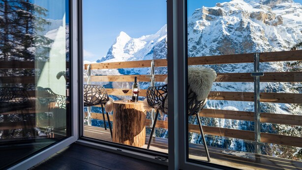 A wooden deck with a table and chairs, overlooking a snow-covered mountain. - Hotel Edelweiss Superior (Mürren)