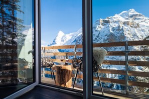 Une terrasse en bois avec une table et des chaises, donnant sur une montagne enneigée.