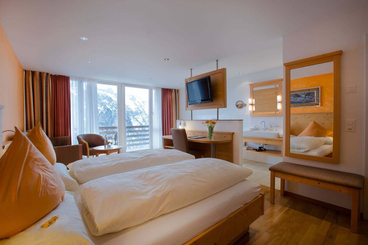 A hotel room with two beds, a desk, a chair, a TV, and a large mirror.