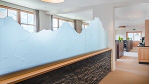 A reception area with a mountain-themed wall, a stone accent wall, and a wooden reception desk. - Hotel Edelweiss Superior (Mürren)