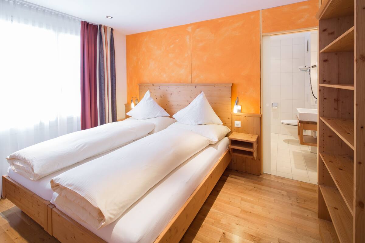A double bed with white linens in a room with wooden flooring and an orange accent wall.