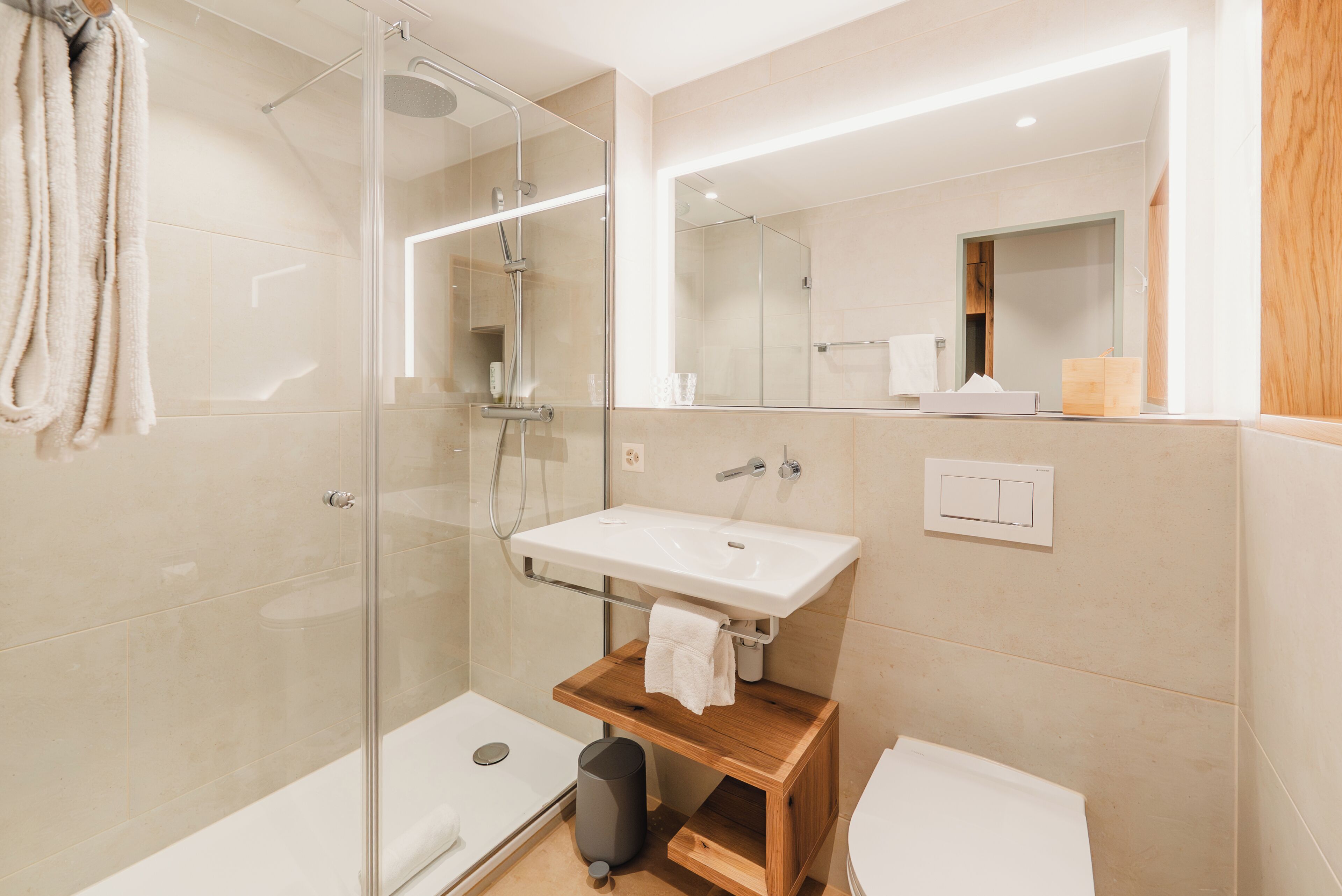 Un baño moderno con cabina de ducha de vidrio, un lavamanos blanco y un mueble de tocador de madera.