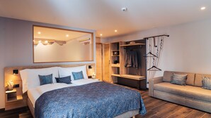 A modern bedroom with a large bed, a sofa, a wardrobe, and a mirror. - Hotel Edelweiss Superior (Mürren)
